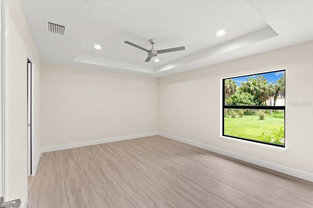 unfurnished room with light hardwood / wood-style floors, a tray ceiling, and ceiling fan