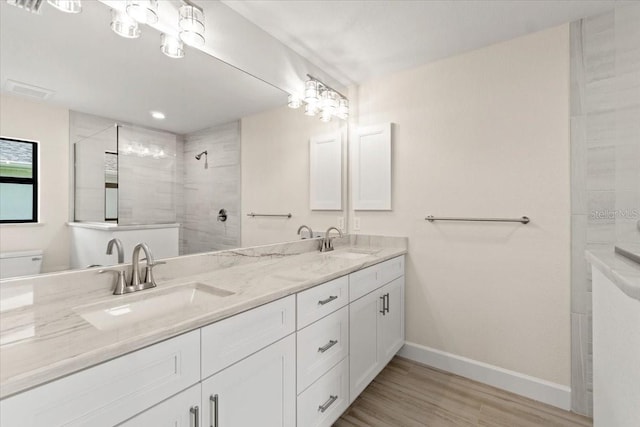 bathroom with toilet, hardwood / wood-style floors, vanity, and a tile shower