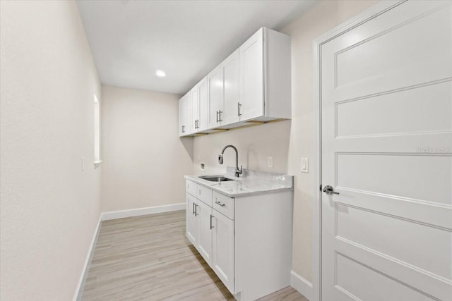 interior space featuring light hardwood / wood-style floors, white cabinets, light stone counters, and sink