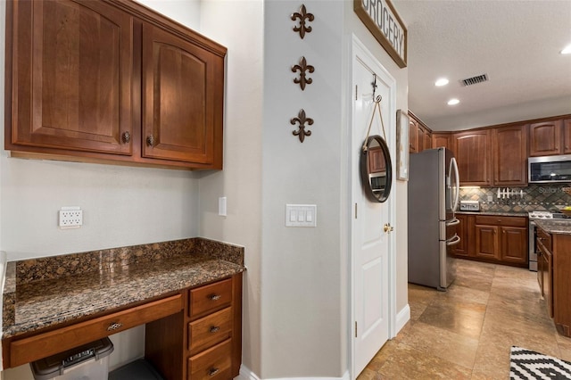 kitchen featuring dark stone counters, decorative backsplash, stainless steel appliances, and a textured ceiling