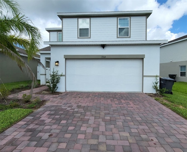 traditional-style home featuring decorative driveway, an attached garage, and stucco siding