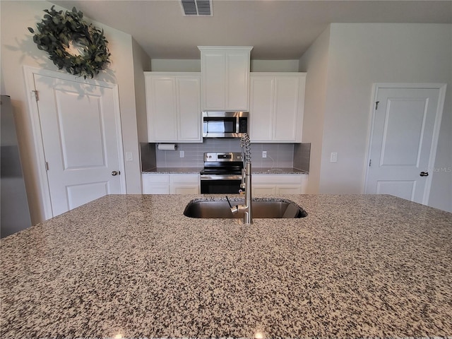 kitchen featuring visible vents, decorative backsplash, appliances with stainless steel finishes, white cabinets, and a sink