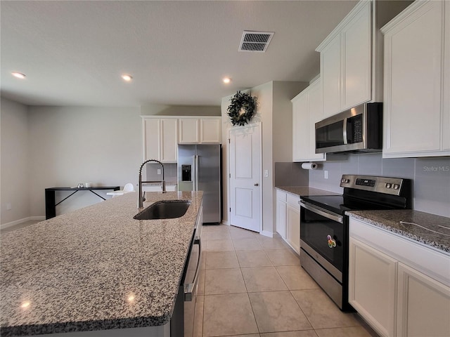 kitchen featuring visible vents, an island with sink, appliances with stainless steel finishes, white cabinetry, and a sink