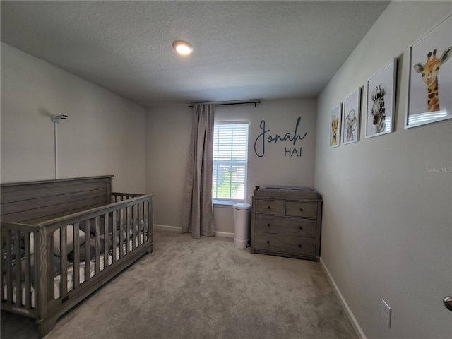 bedroom featuring a nursery area, carpet, baseboards, and a textured ceiling