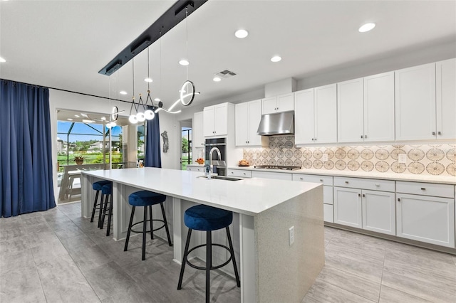 kitchen with decorative light fixtures, sink, white cabinets, and a kitchen island with sink