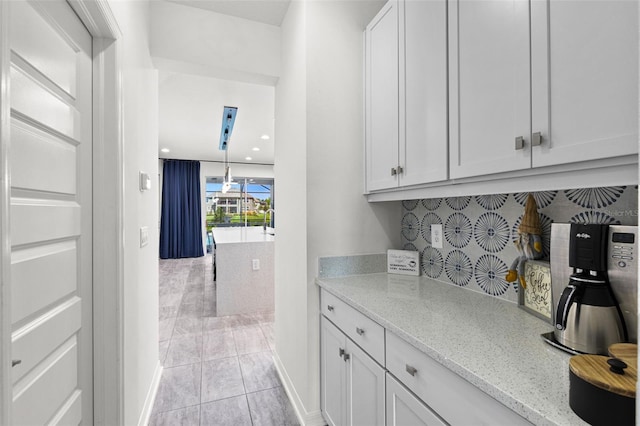 interior space featuring light tile patterned floors, decorative backsplash, white cabinets, and light stone counters