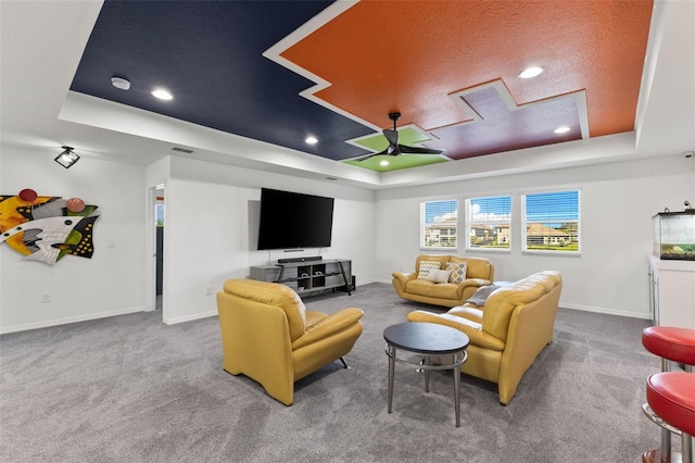 carpeted living room with ceiling fan and a raised ceiling