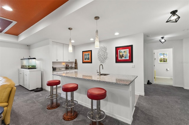 kitchen featuring a kitchen bar, hanging light fixtures, light stone countertops, white cabinets, and sink