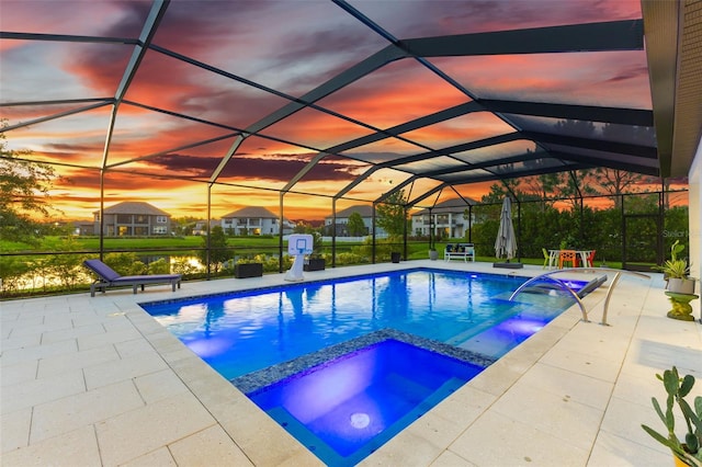 pool at dusk with a water view, a patio area, glass enclosure, and an in ground hot tub