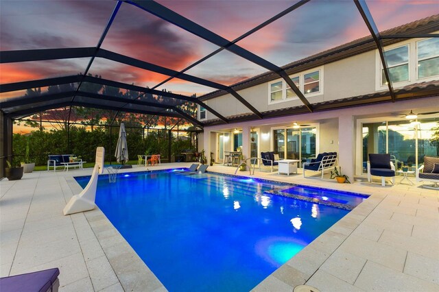 pool at dusk featuring a lanai, ceiling fan, and a patio area