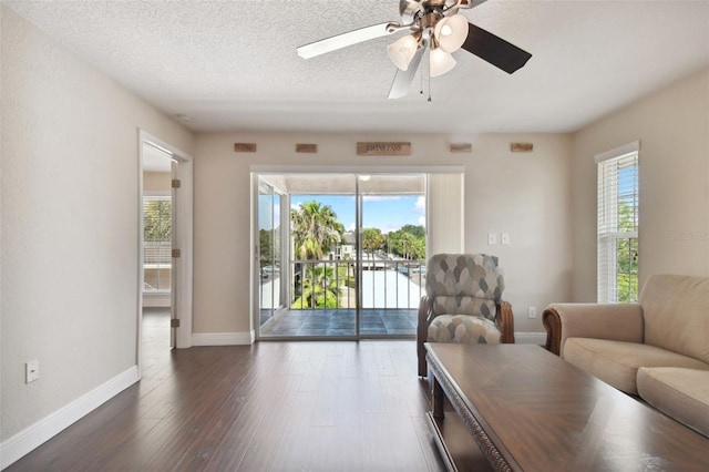 living room featuring dark wood-type flooring, ceiling fan, a healthy amount of sunlight, and a textured ceiling