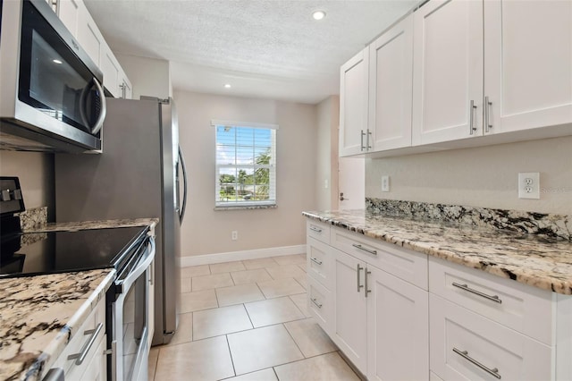 kitchen featuring light tile patterned flooring, appliances with stainless steel finishes, white cabinets, light stone counters, and a textured ceiling