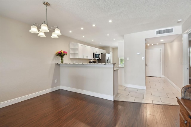 kitchen with stainless steel appliances, white cabinets, decorative light fixtures, kitchen peninsula, and light wood-type flooring