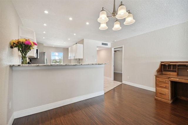 kitchen featuring dark wood-type flooring, white cabinetry, light stone counters, stainless steel fridge, and kitchen peninsula