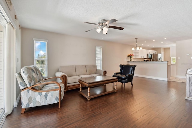 living room with dark wood-type flooring, ceiling fan with notable chandelier, and a textured ceiling