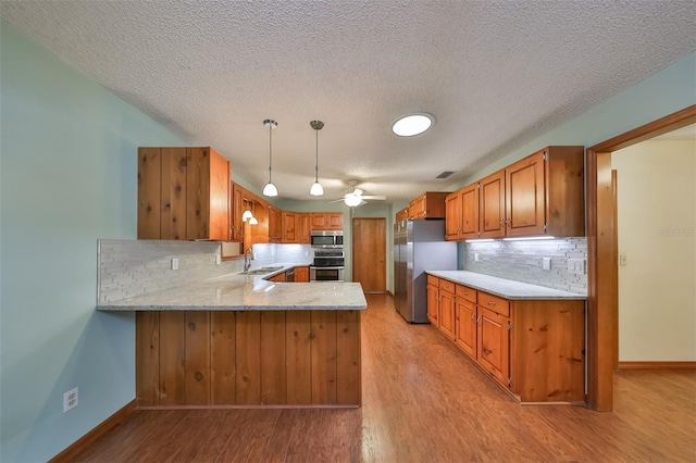 kitchen with pendant lighting, stainless steel appliances, sink, backsplash, and kitchen peninsula