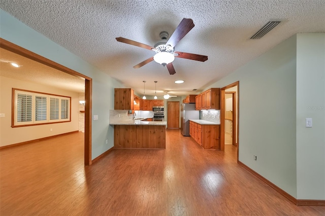 kitchen featuring appliances with stainless steel finishes, decorative light fixtures, decorative backsplash, kitchen peninsula, and ceiling fan