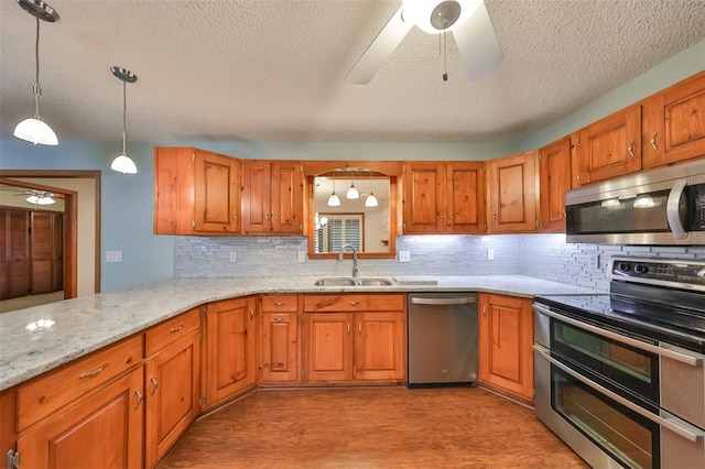 kitchen with appliances with stainless steel finishes, sink, hanging light fixtures, kitchen peninsula, and ceiling fan