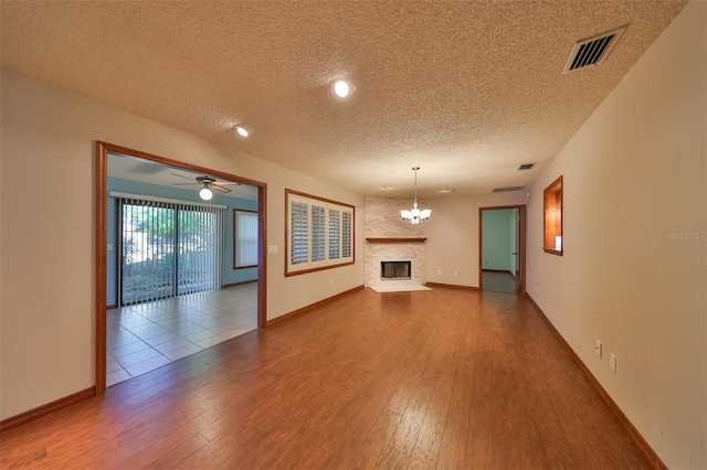 unfurnished living room with ceiling fan with notable chandelier, a textured ceiling, hardwood / wood-style flooring, and a large fireplace