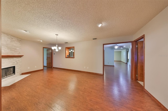 unfurnished living room featuring ceiling fan with notable chandelier, a stone fireplace, hardwood / wood-style floors, and a textured ceiling