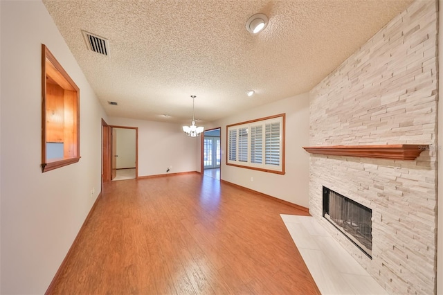 unfurnished living room with light wood-type flooring, a stone fireplace, a notable chandelier, and a textured ceiling