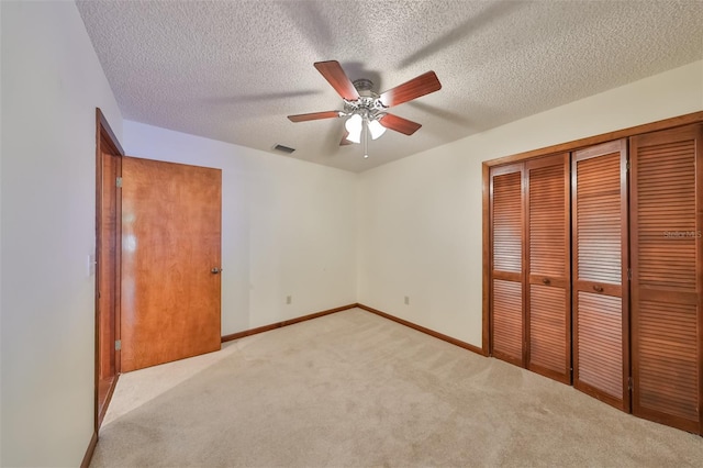 unfurnished bedroom featuring ceiling fan, light colored carpet, a textured ceiling, and a closet