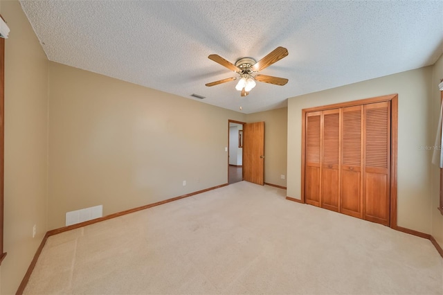 unfurnished bedroom featuring light colored carpet, a textured ceiling, a closet, and ceiling fan