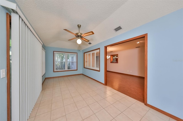 unfurnished room with a textured ceiling, ceiling fan with notable chandelier, light tile patterned floors, and lofted ceiling