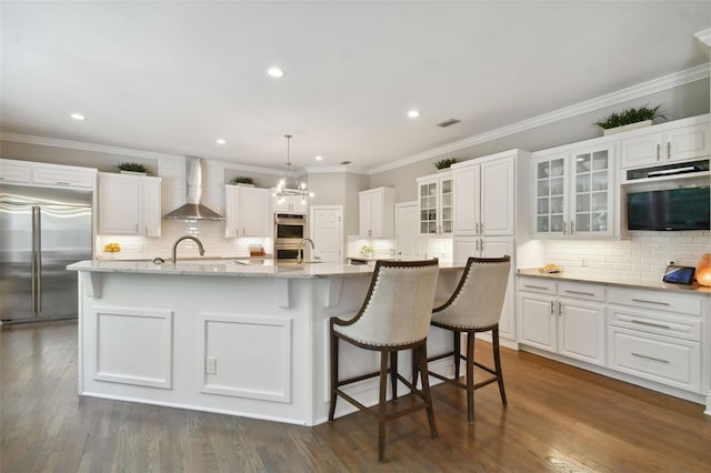 kitchen featuring an island with sink, wall chimney exhaust hood, tasteful backsplash, and stainless steel built in refrigerator