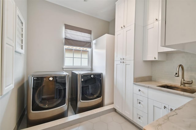 clothes washing area with washer and clothes dryer, sink, light tile flooring, and cabinets