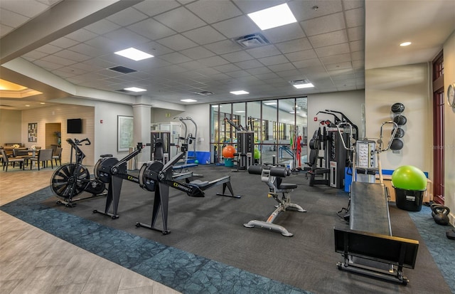 gym featuring a paneled ceiling and decorative columns