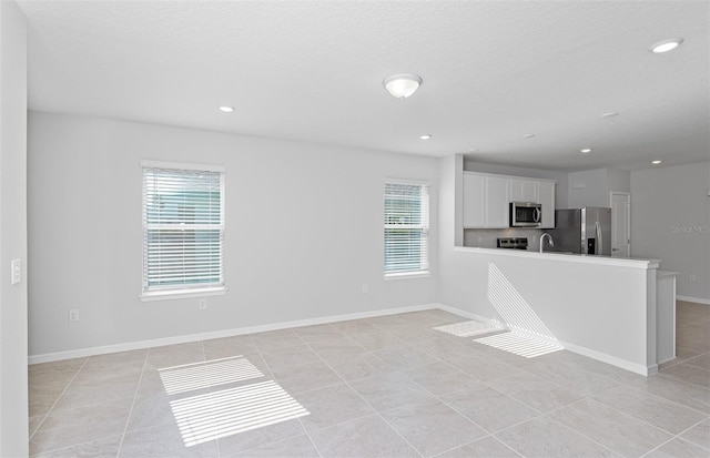 interior space with a textured ceiling, stainless steel appliances, light tile patterned floors, and white cabinetry