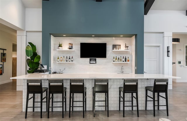 bar featuring a towering ceiling, sink, and dark hardwood / wood-style flooring