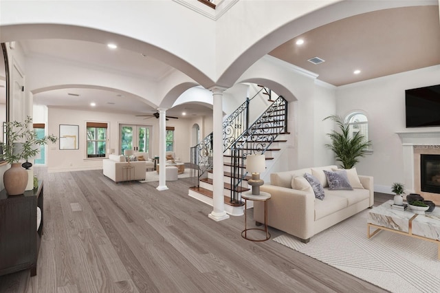 living room with light wood-type flooring, ornamental molding, ceiling fan, a premium fireplace, and decorative columns