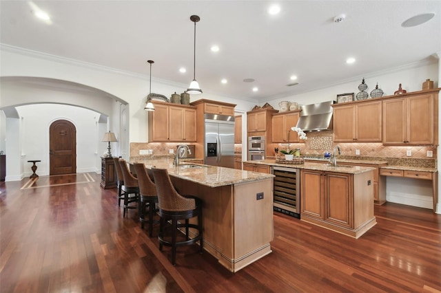 kitchen with sink, beverage cooler, hanging light fixtures, stainless steel appliances, and wall chimney exhaust hood