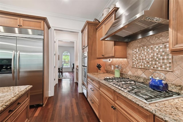 kitchen featuring light stone countertops, appliances with stainless steel finishes, wall chimney range hood, and dark hardwood / wood-style flooring