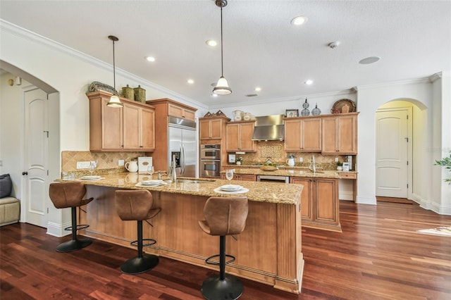 kitchen featuring arched walkways, dark wood-type flooring, a peninsula, stainless steel appliances, and wall chimney range hood