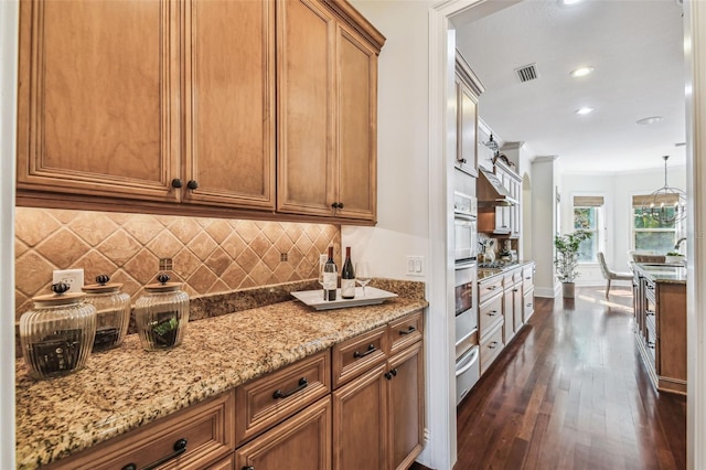 kitchen featuring tasteful backsplash, visible vents, brown cabinetry, dark wood-style flooring, and light stone countertops