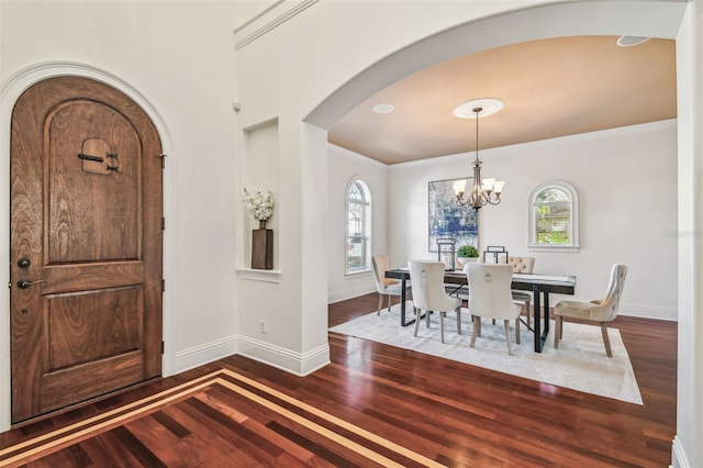 interior space featuring arched walkways, crown molding, an inviting chandelier, wood finished floors, and baseboards