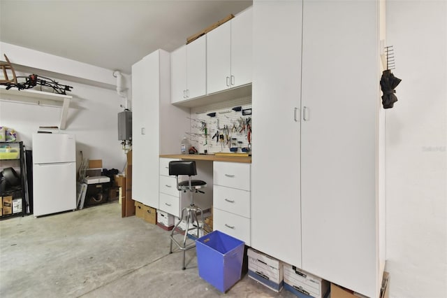 interior space featuring freestanding refrigerator, water heater, white cabinets, and unfinished concrete floors