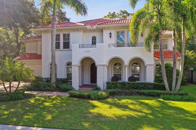 mediterranean / spanish-style house with a front yard, a tiled roof, a balcony, and stucco siding