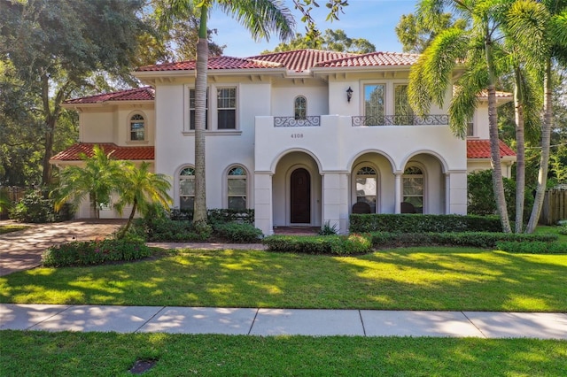 mediterranean / spanish-style home with stucco siding, a front yard, a balcony, a garage, and a tiled roof