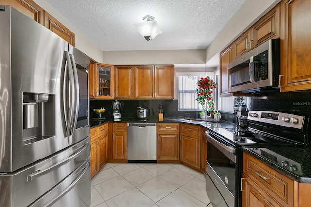 kitchen featuring backsplash, dark stone counters, sink, light tile patterned floors, and stainless steel appliances