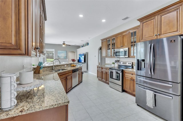 805 Woodcarver Ln, Brandon, FL 33510 - kitchen with appliances with stainless steel finishes, brown cabinetry, a peninsula, light stone countertops, and ceiling fan