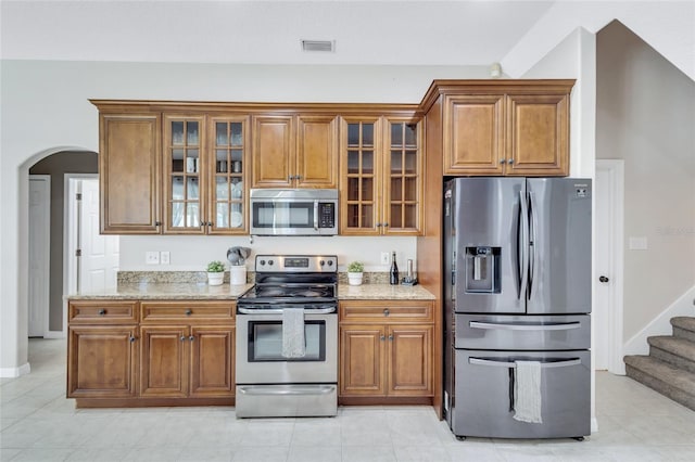 805 Woodcarver Ln, Brandon, FL 33510 - kitchen featuring stainless steel appliances, brown cabinetry, light stone countertops, and arched walkways