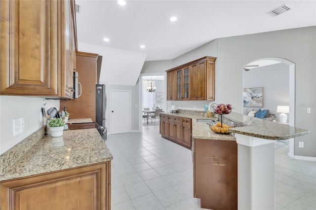 805 Woodcarver Ln, Brandon, FL 33510 - kitchen with a peninsula, brown cabinets, light tile patterned floors, freestanding refrigerator, and arched walkways