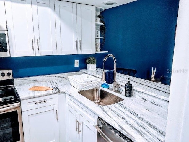 kitchen with white cabinets, appliances with stainless steel finishes, sink, and light stone countertops