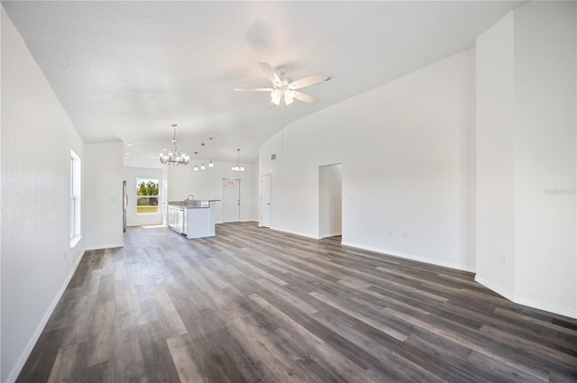 unfurnished living room with ceiling fan with notable chandelier, dark wood-style flooring, and baseboards