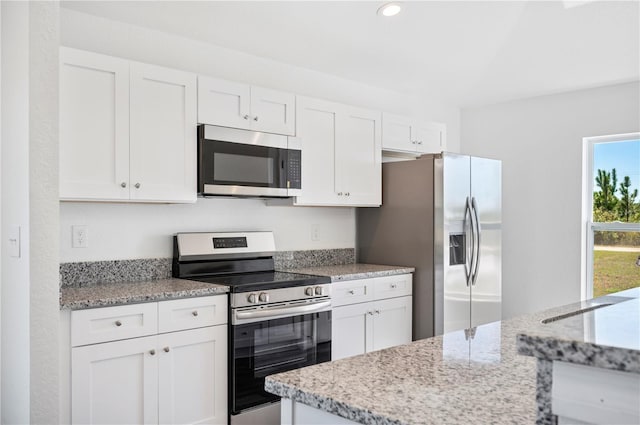 kitchen with appliances with stainless steel finishes, white cabinets, a sink, and light stone counters