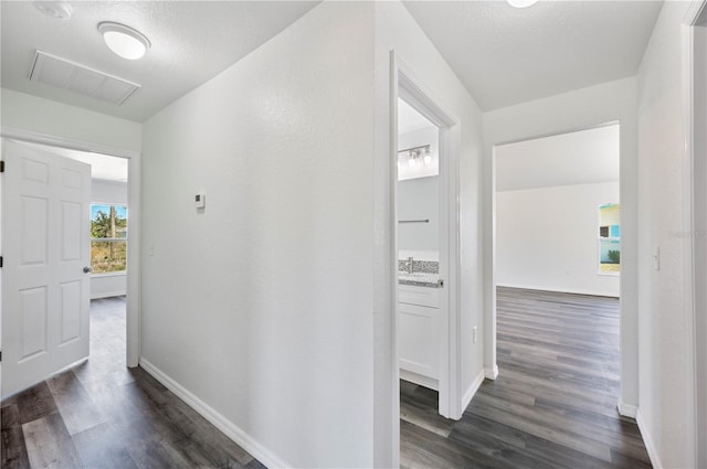 hallway with visible vents, dark wood finished floors, a sink, and baseboards